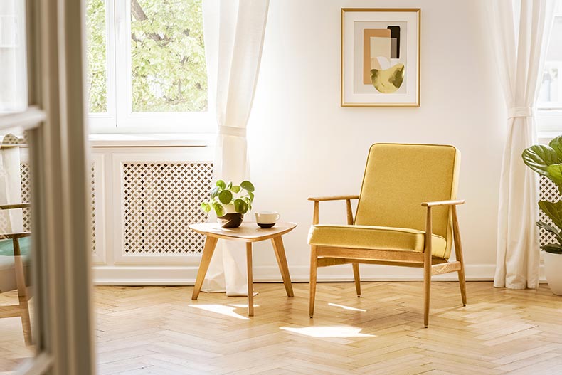 A retro, yellow armchair and a wooden table in a beautiful, sunny living room.