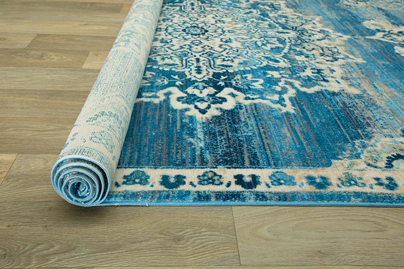 Rolling out a blue rug on a wood floor.