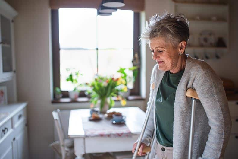 A 55+ woman with crutches at home in her kitchen.