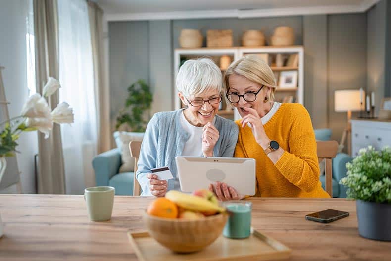 Two 55+ women using a credit card for online shopping.