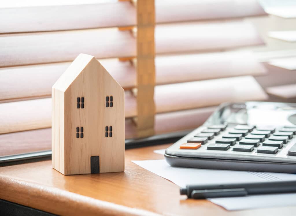 A wooden house model, a calculator, and a notebook on an office desk.