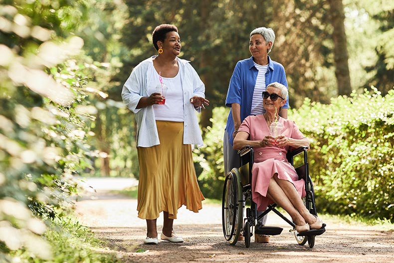 A group of 55+ women enjoying a walk in a park together with one in a wheelchair.