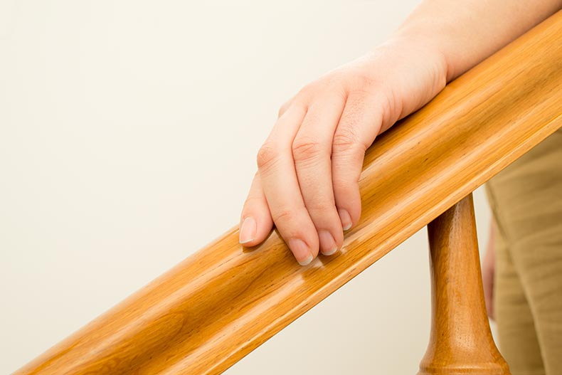 Closeup of a 55+ woman using a railing to go downstairs at home.