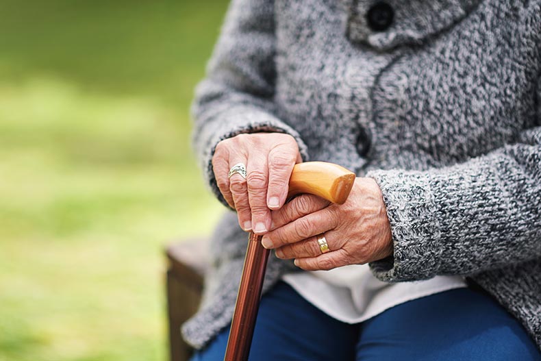 A 55+ woman holding a cane while sitting on a park bench.