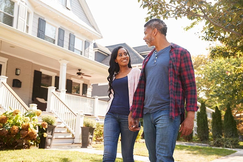 A 55+ couple walking along a suburban street holding hands.