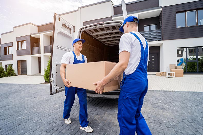 Two moving company workers unloading boxes and furniture from a minibus.