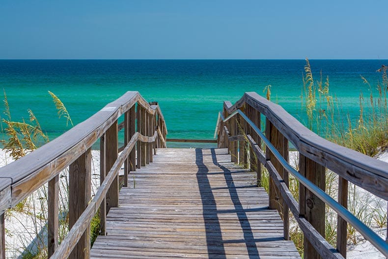 A wooden boardwalk leading to Pensacola Beach on a sunny day.