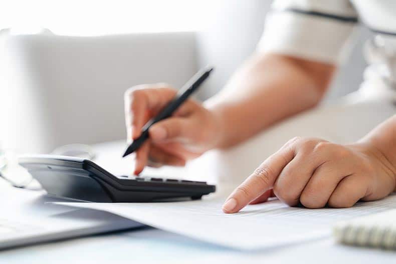 Active adult woman is calculating her homebuying budget with a calculator.