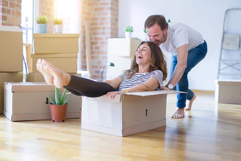 A 55+ couple having fun riding inside of a cardboard box while packing to move.