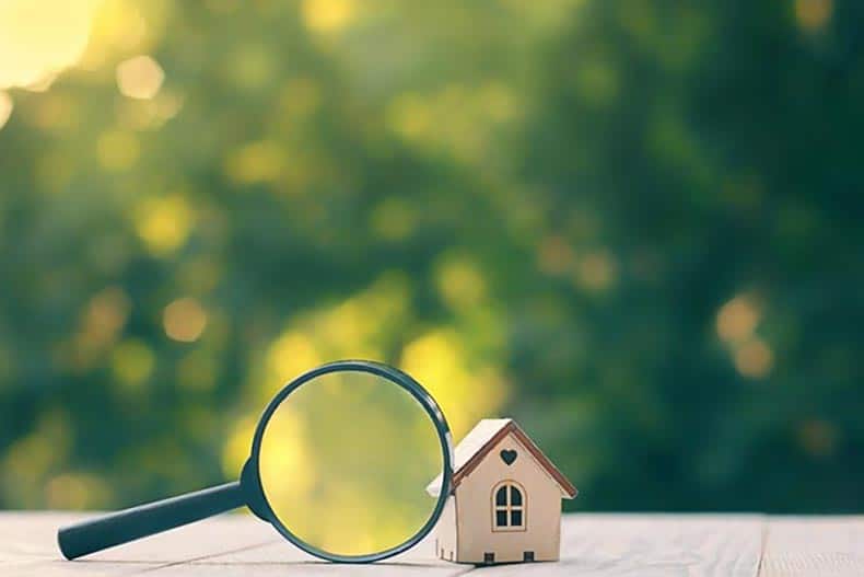 A magnifying glass on a wood table beside a model wood house.