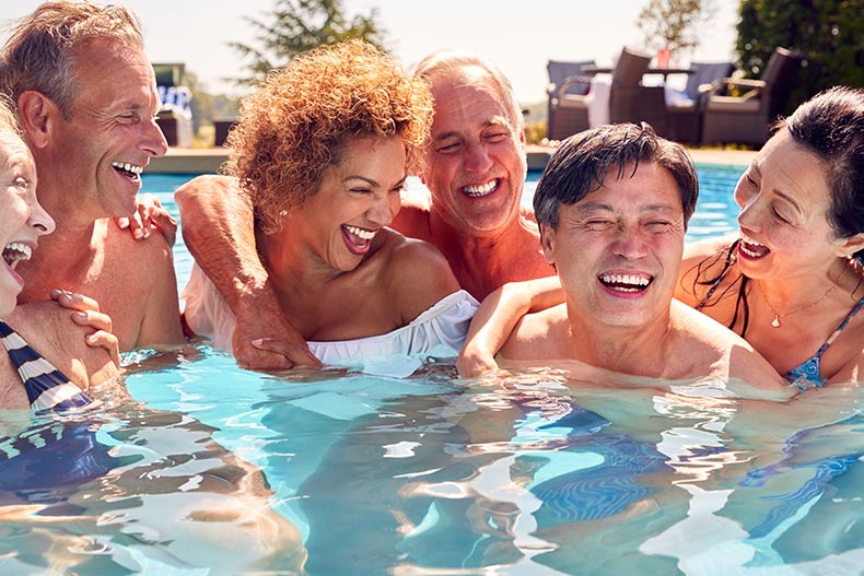 A group of friends smiling and laughing in the outdoor pool at their 55+ community.