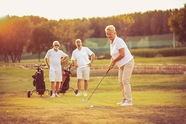 Three 55+ golfers on a golf course at sunset.