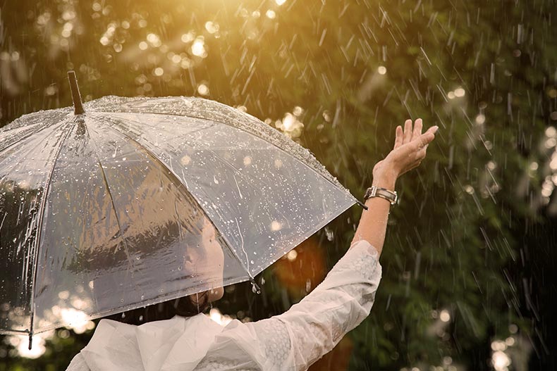 A 55+ woman with an umbrella raising her hand to touch falling rain in Florida.