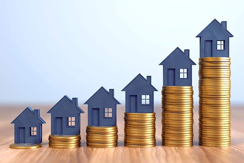 Tiny house silhouettes sitting on stacks of gold coins.