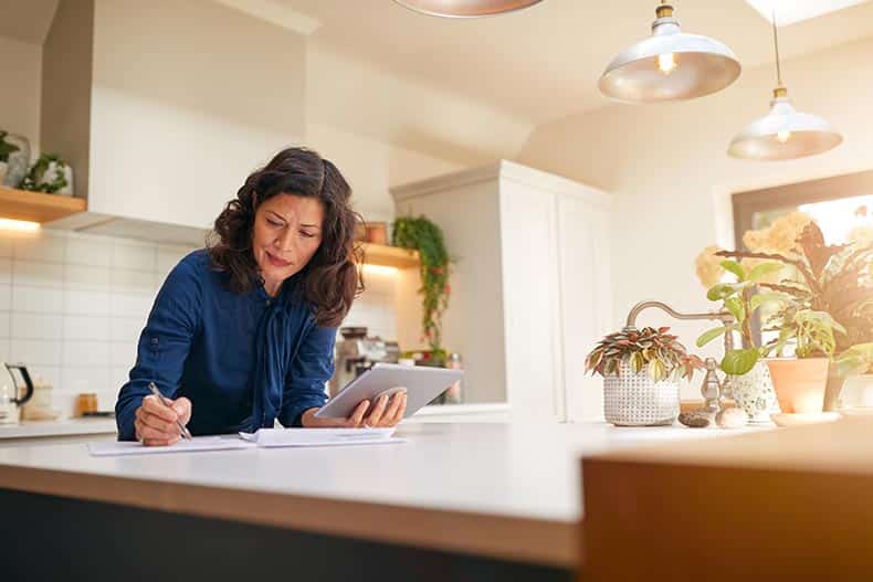 A 55+ woman reviewing her home insurance documents at her kitchen counter.