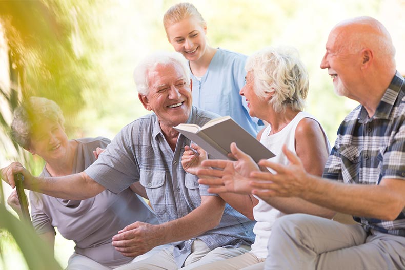 Happy seniors in a nursing home spending time outside and reading a book together.