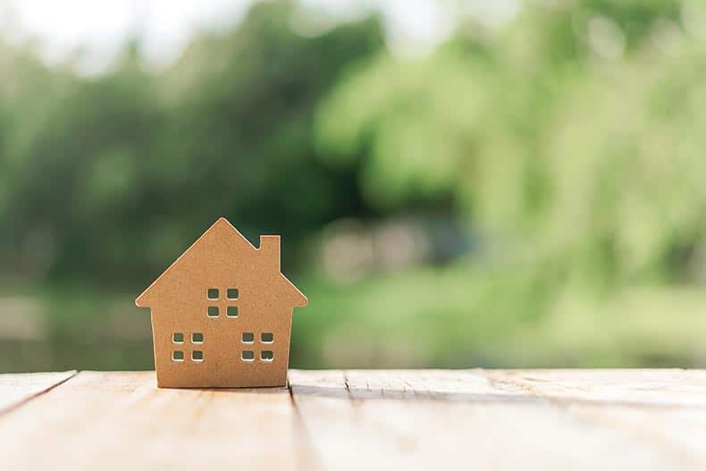 A small home model on a wooden table with a nature background.