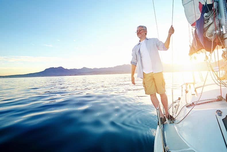 A 55+ man sailing on a boat at sunrise.