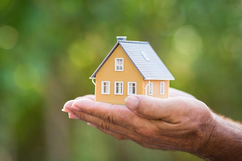 Hands holding a small model house.