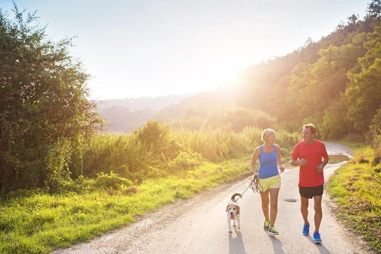 Active seniors running with their dog outside on a nature trail.