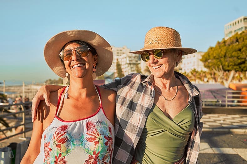 Senior female friends smiling and laughing at the beach.