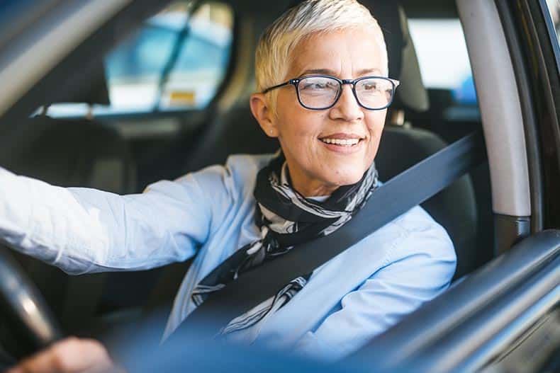 A 55+ woman driving in her car with the window rolled down.