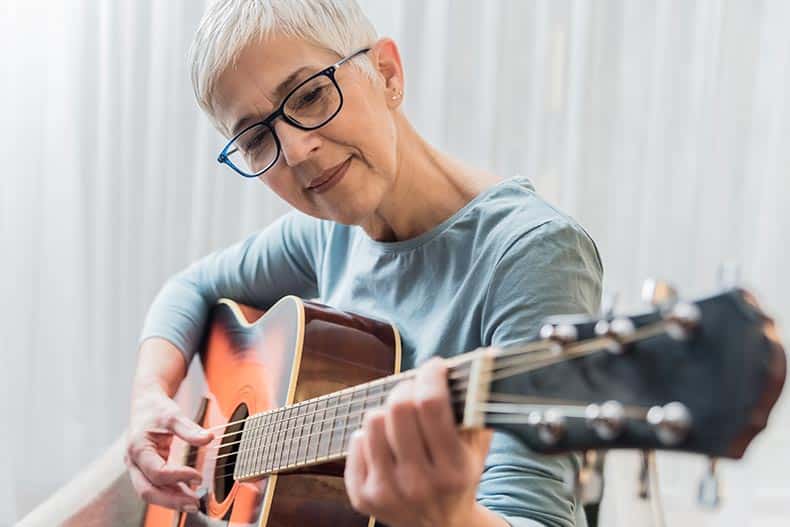 Closeup of a 55+ woman practicing guitar.