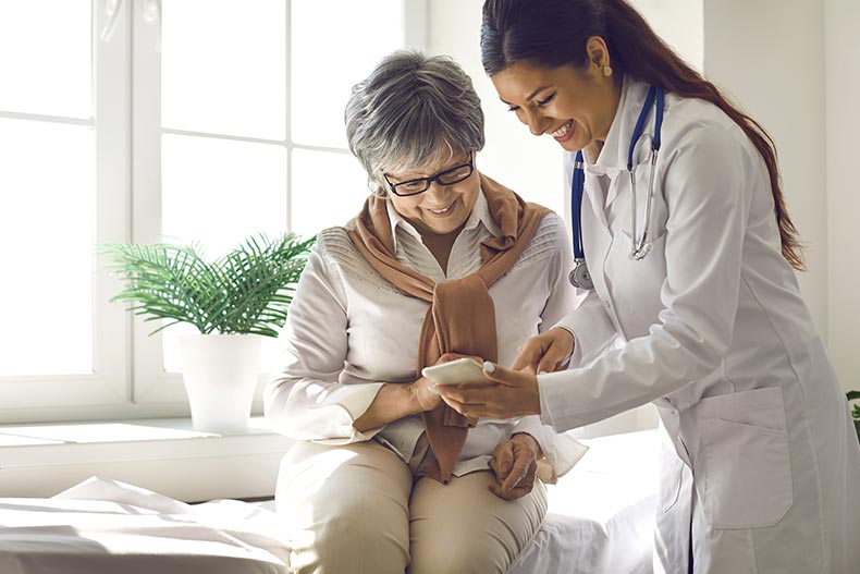 A caring doctor teaches female 55+ patient to use a mobile health care app.