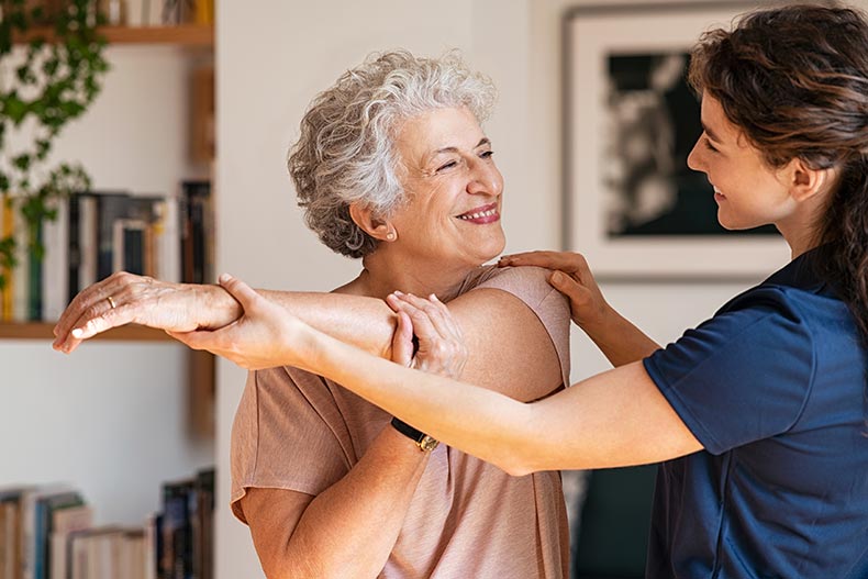 A happy senior woman doing exercises at home with a physiotherapist.