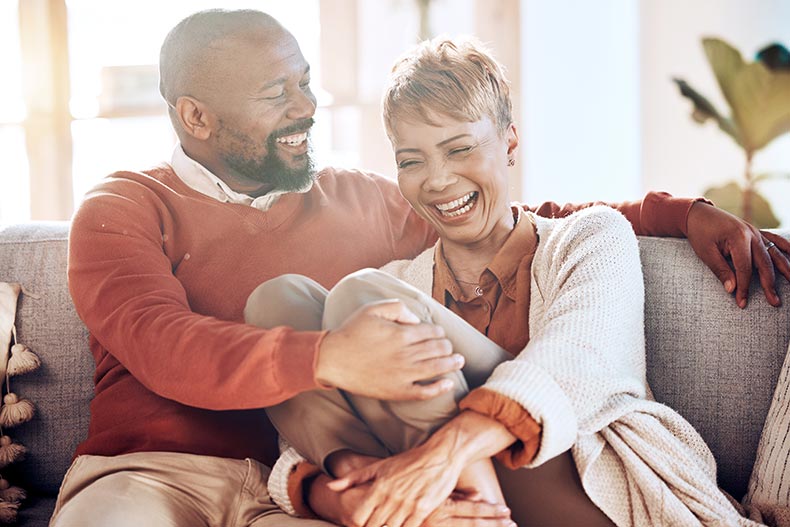 A happy 55+ couple laughing on their living room sofa.