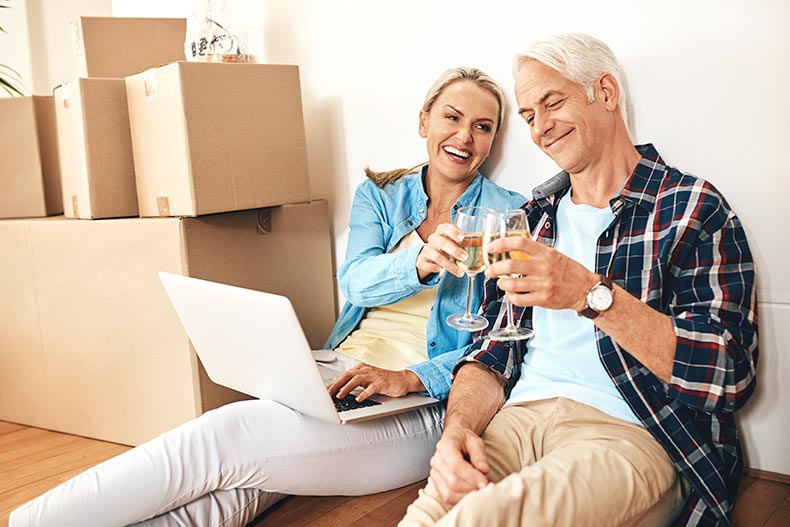 A happy 55+ couple using a laptop and drinking wine together on moving day.