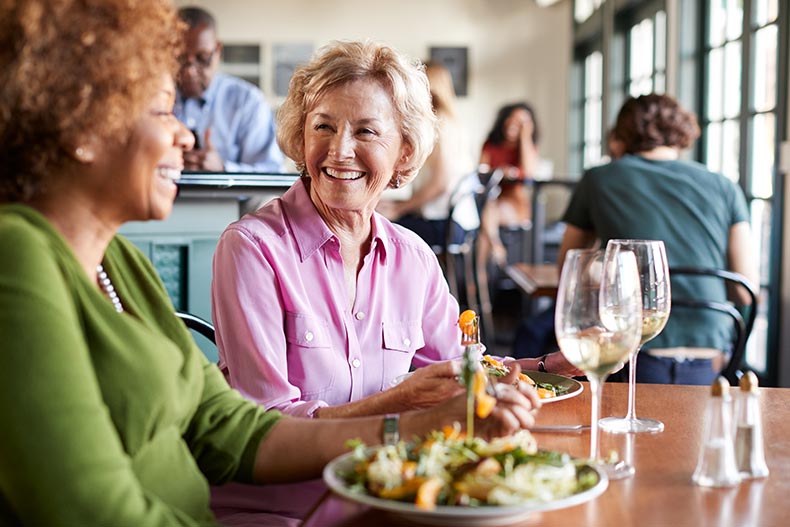Two smiling 55+ women meeting for a meal in restaurant.