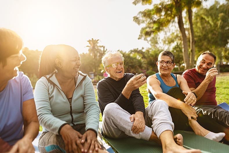 Active adult friends drinking a tea after workout activities in a park in their 55+ community.