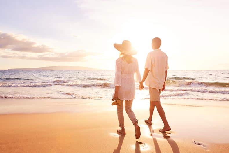 A happy 55+ couple enjoying a walk on the beach in Florida at sunset.