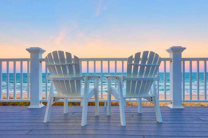 Empty Adirondack chairs on a deck overlooking the beach and the ocean at sunset.