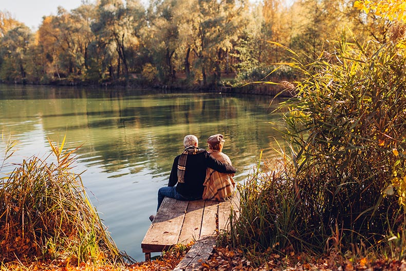 A 55+ couple relaxing by a lake in autumn.