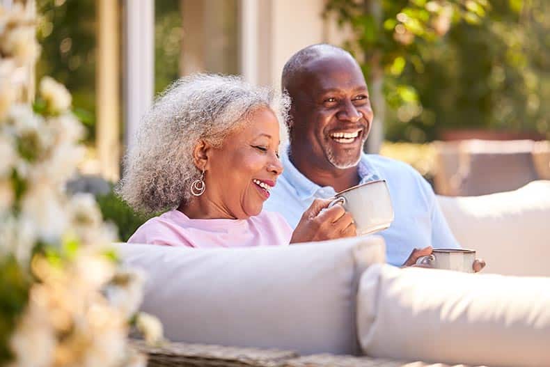 A retired couple sitting outdoors at home having morning coffee together.