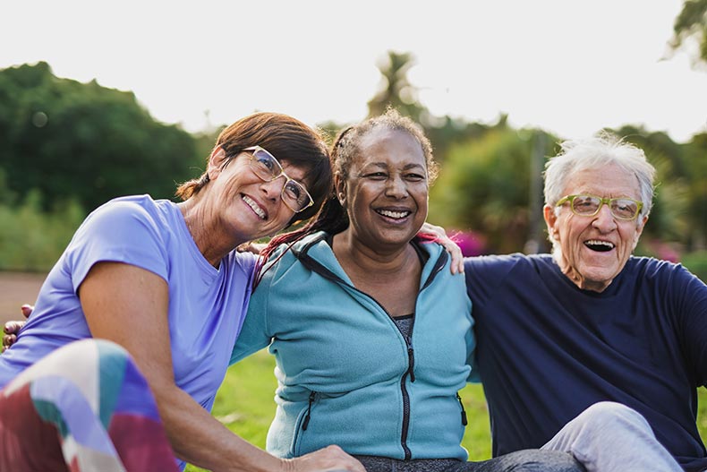 Happy active adults hugging each other after an outdoor yoga lesson in their 55+ community.