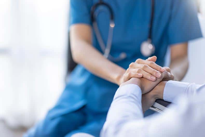 A female nurse holding a senior patient's hand.