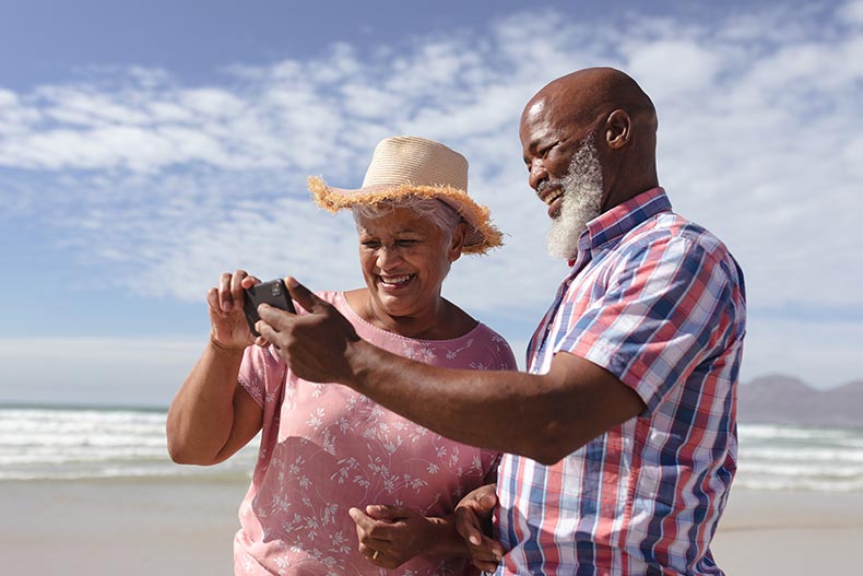 A happy 55+ couple using a smartphone at the beach.