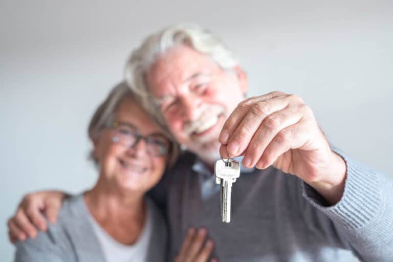 A retired couple hold up their new keys after completing their homebuying process.