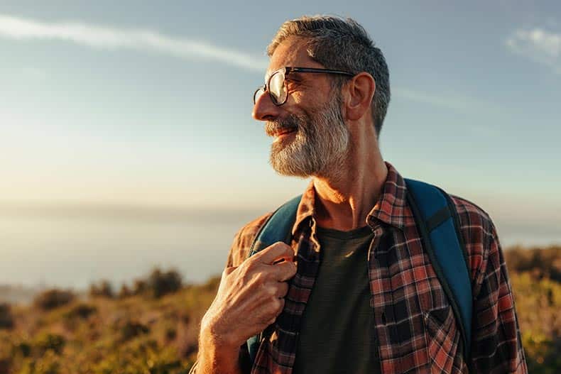 55+ hiker standing on top of a hill with a backpack.