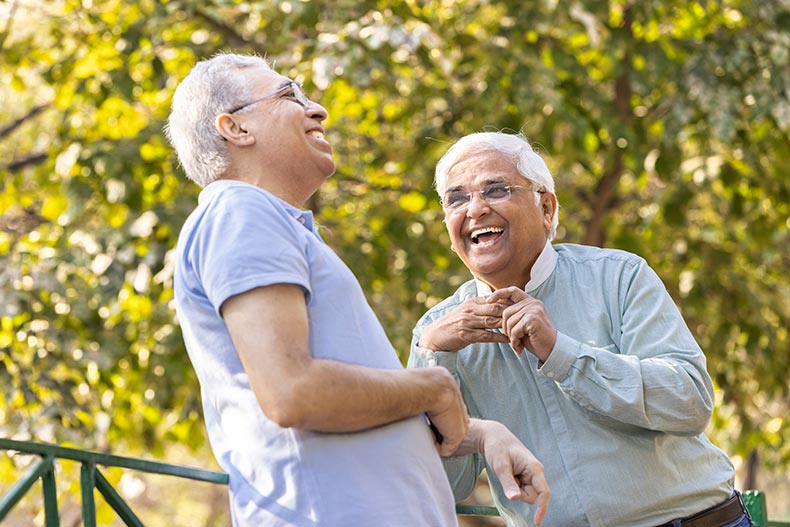 Two 55+ men talking and laughing outside on a sunny day.