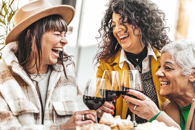 A group of 55+ women laughing while enjoying a glass of wine together.