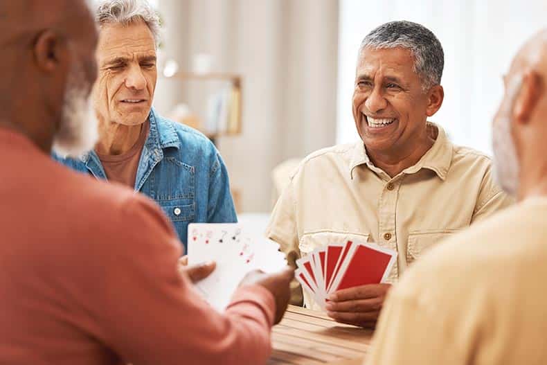 55+ friends playing card games at a wooden table.