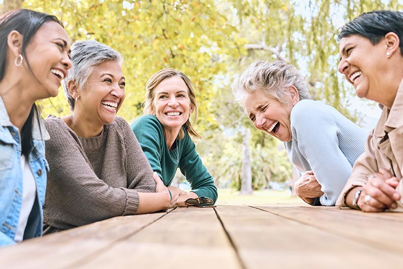 A group of female friends laughing together at a park table in their 55+ community.