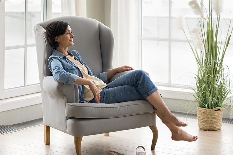 A 55+ woman sitting in an armchair in the living room of her home.