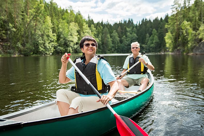 Happy 55+ couple in life vests canoeing in forest lake.