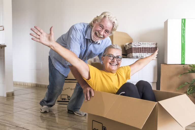 Older couple plays with boxes while packing to move.