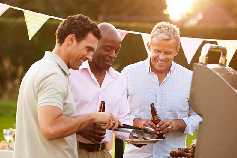 55+ male neighbors enjoying a summer barbecue outdoors.